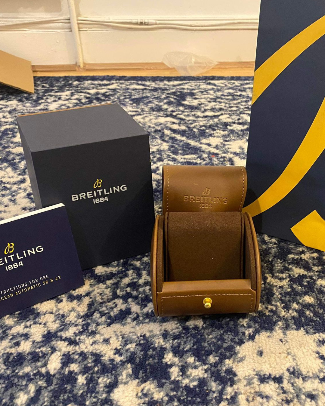 Breitling Watch Box with brown leather storage case and branded packaging on a carpeted floor
