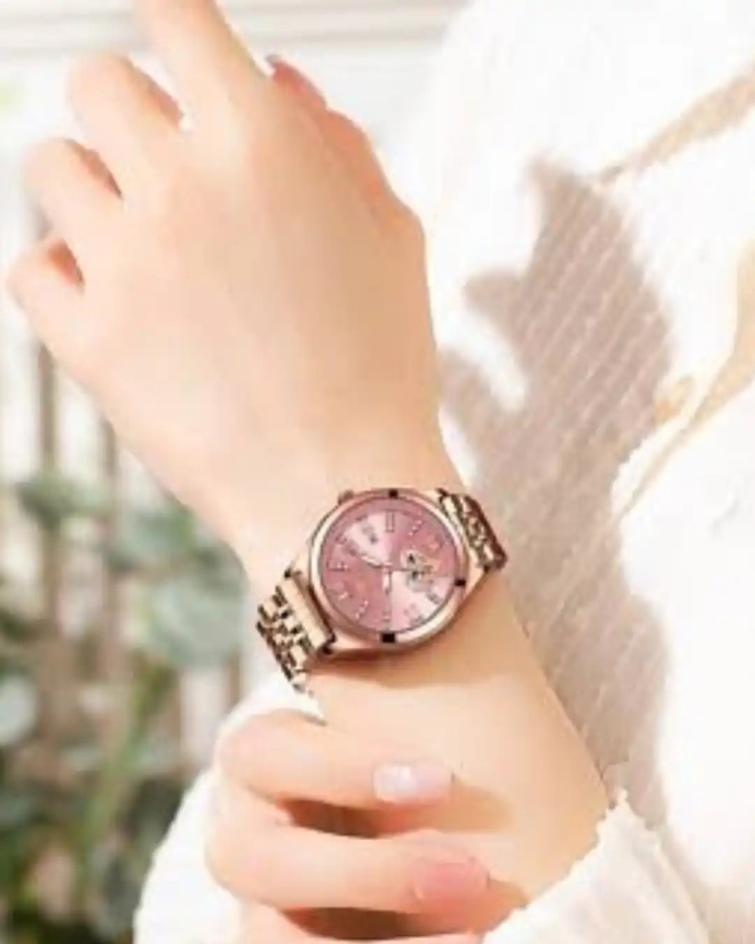 A rose gold women’s wristwatch with a pink face and Roman numeral hour markers.